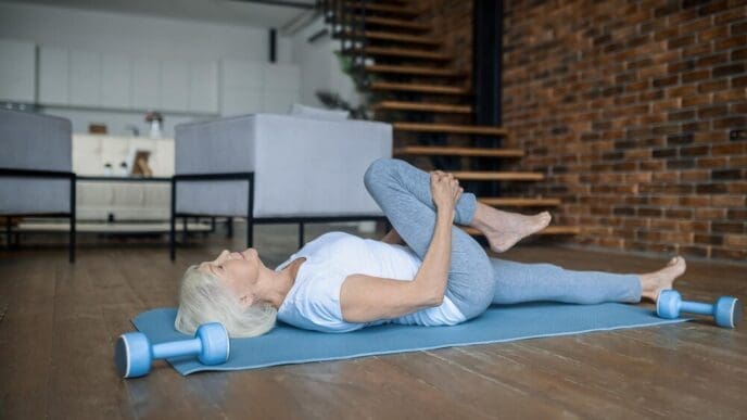An elderly woman wearing workout clothes practices yoga in her home.