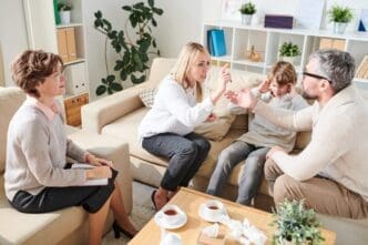 A young boy sits on a couch, watching his parents argue with each other during a therapy session.