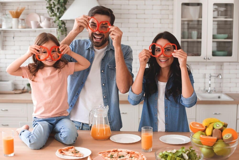 A family holds bell pepper rings over their eyes and smiles at the camera.