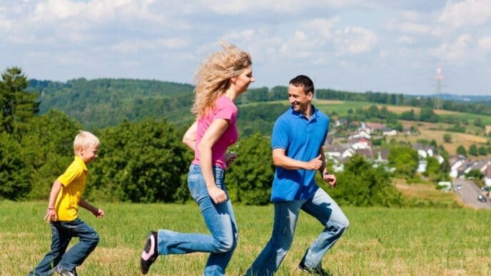 A family is joyfully playing tag in a grassy meadow on a sunny day.
