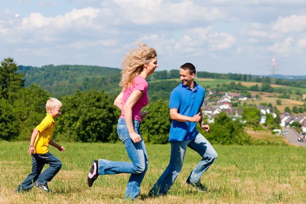 A family is joyfully playing tag in a grassy meadow on a sunny day.