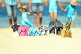 Family slippers arranged on a sandy beach in the summer sun.