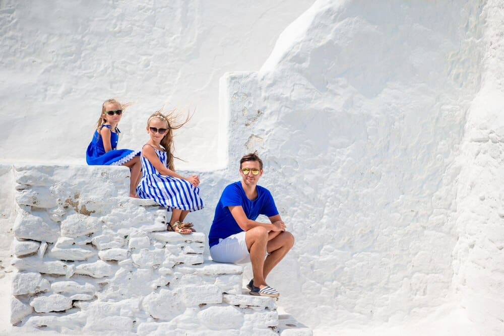 A family of three stands on the stairs of the whitewashed Paraportiani church on Mykonos Island, Greece.