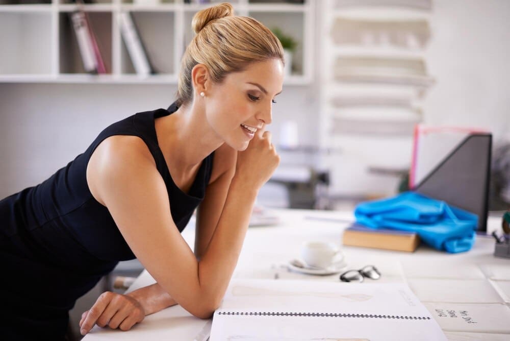 A fashion designer sketches ideas for clothing production at her desk in a workshop.