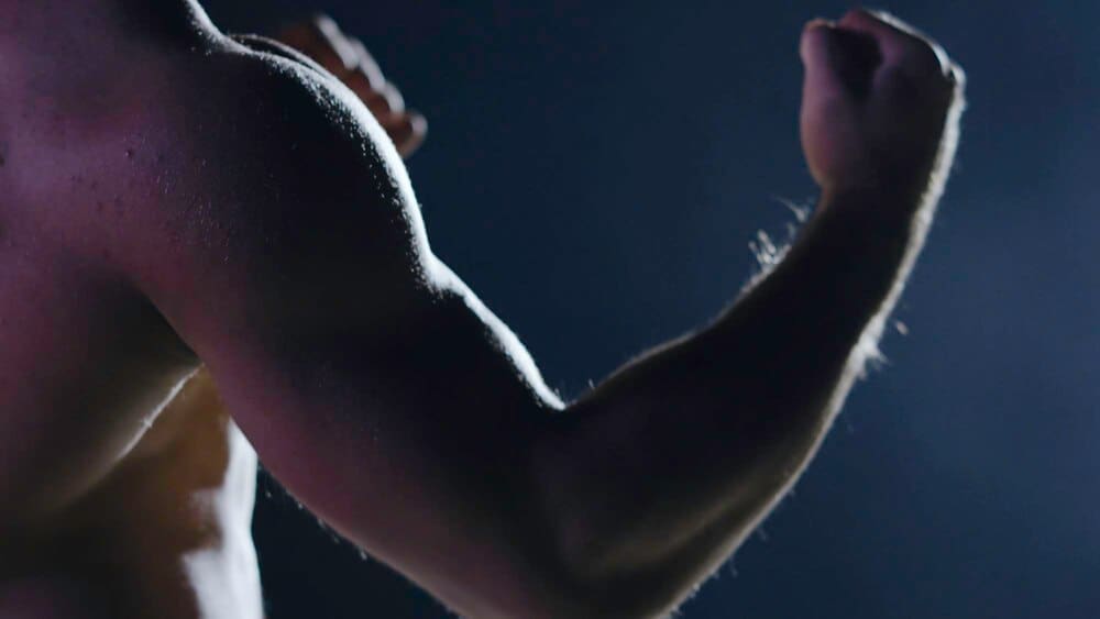 Silhouette of a muscular, athletic man in a boxing stance against a dark background.