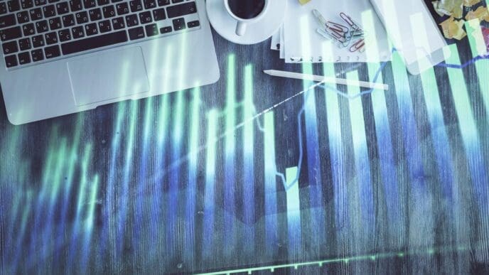 A financial market graph is superimposed over a top-down view of a computer on a desktop, illustrating the concept of investment.