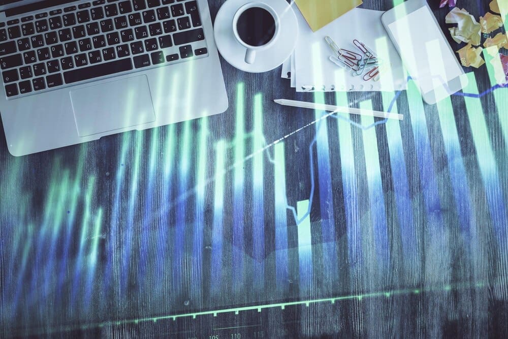 A financial market graph is superimposed over a top-down view of a computer on a desktop, illustrating the concept of investment.