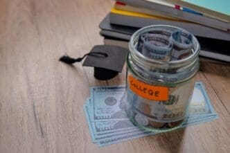 A hand places coins into a piggy bank, symbolizing saving money for college.