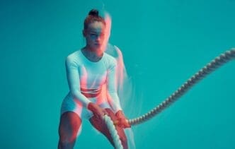 A fitness model on a blue background exercises with a rope, performing a fat-burning workout.