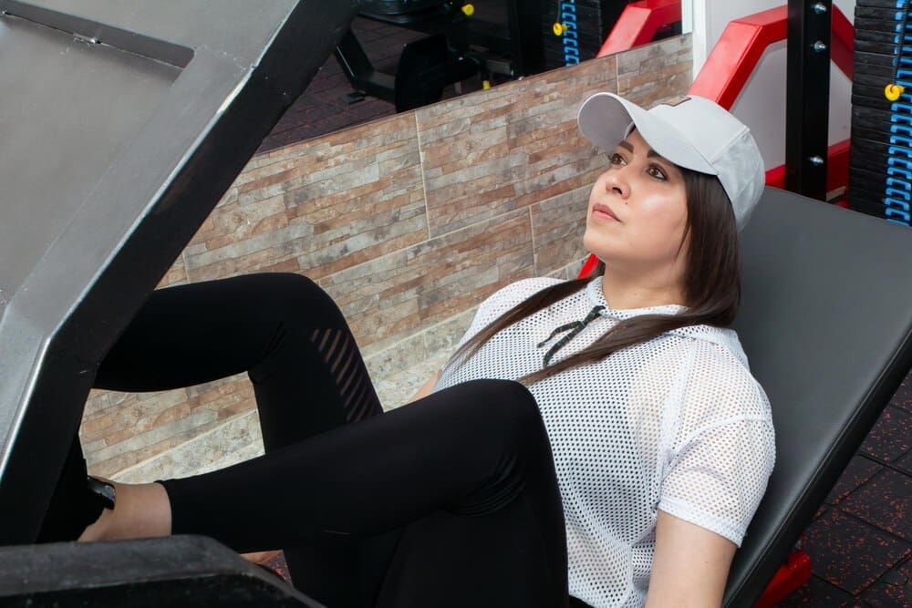 A woman uses a weight machine to do a leg exercise in a gym.