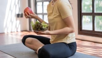 Woman in workout clothes eating a salad in a yoga studio.