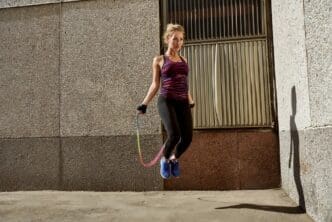 A woman in fitness attire jumps in an urban environment.