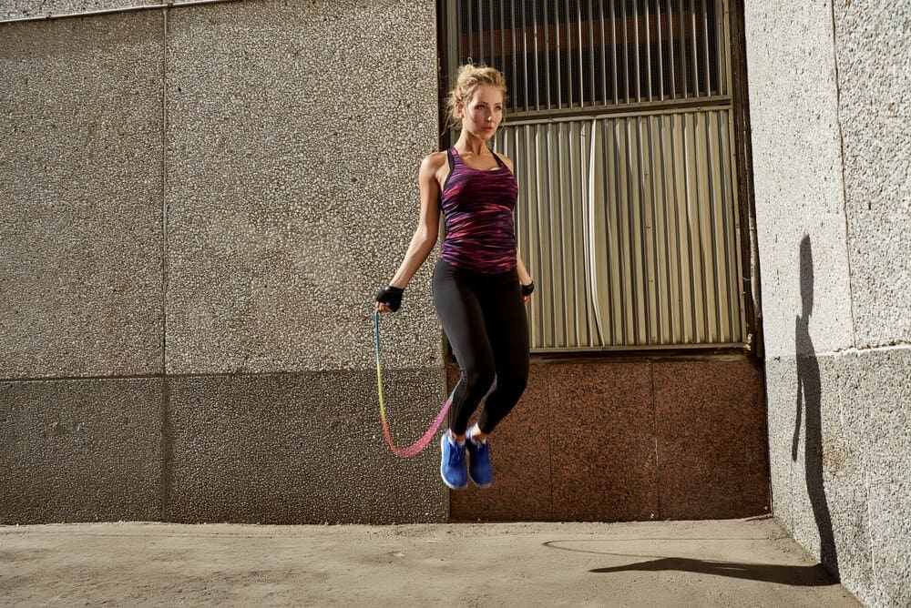 A woman in fitness attire jumps in an urban environment.