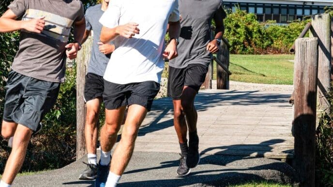 Four cross-country runners in motion, making a left turn while crossing a wooden bridge on a path.