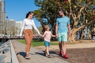 A smiling family, with the parents in front, leads a young boy, all enjoying a sunny summer day.