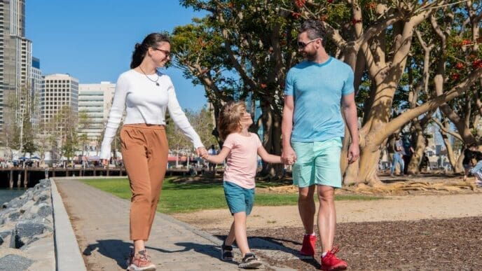 A smiling family, with the parents in front, leads a young boy, all enjoying a sunny summer day.