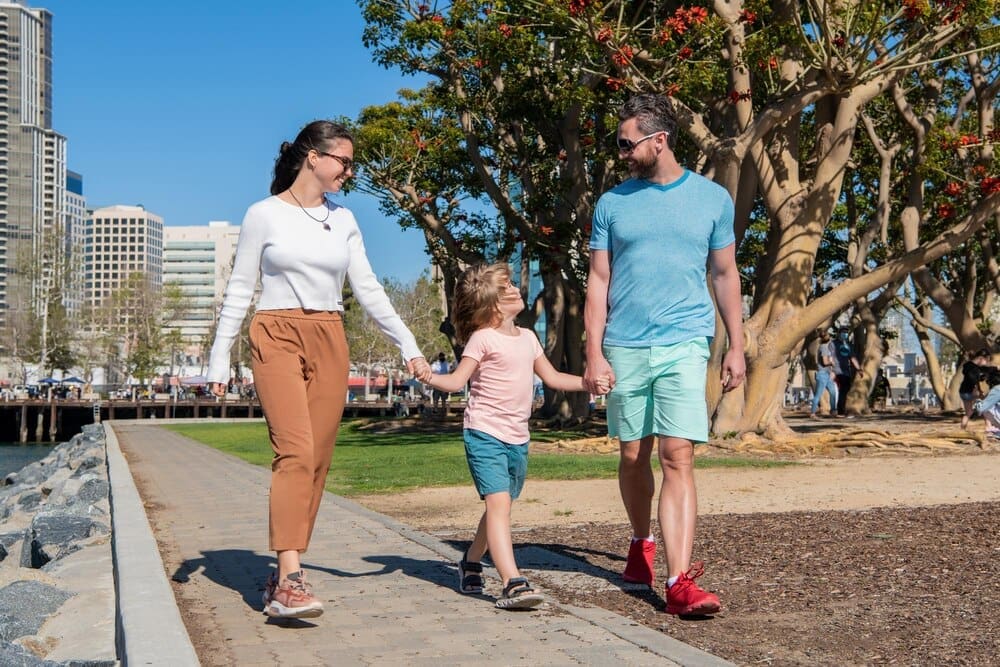 A smiling family, with the parents in front, leads a young boy, all enjoying a sunny summer day.