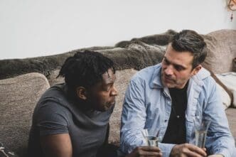 Two friends sit on a drinking glass that a man is holding.