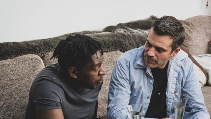 Two friends sit on a drinking glass that a man is holding.