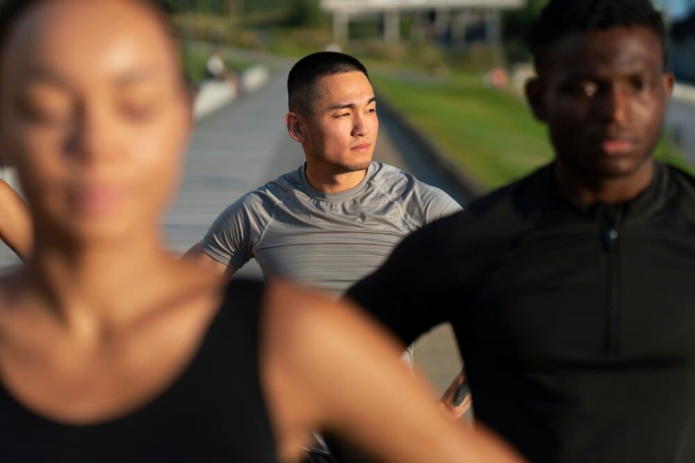 Four friends, dressed in workout clothes, stand together smiling outdoors.