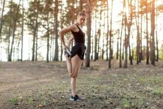 A woman stretches her leg in a forest, demonstrating flexibility.