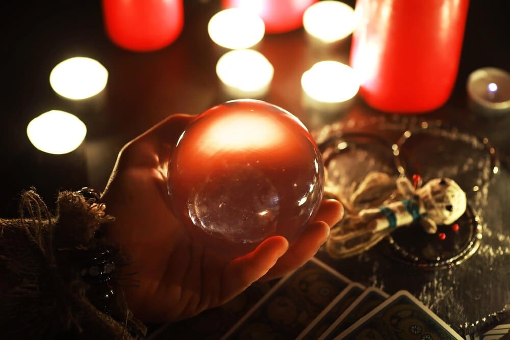 A still life of divination tools includes a voodoo doll, tarot cards, books, candles, and other witchcraft objects.
