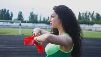 A young girl in a green top prepares to throw a red cup on a track while engaged in aerobics.