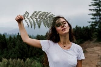 A young girl hikes through a foggy mountain landscape, holding a fern leaf.