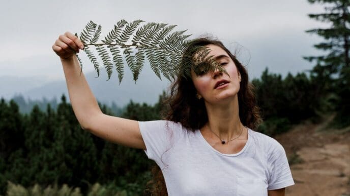 A young girl hikes through a foggy mountain landscape, holding a fern leaf.