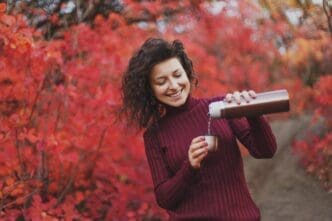 A girl in a red sweater pours tea from a silver thermos.