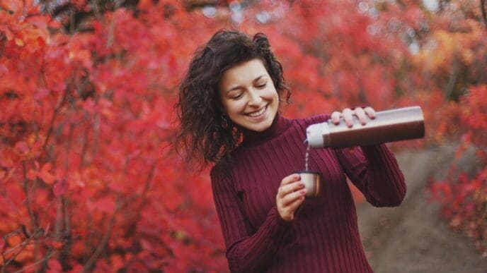 A girl in a red sweater pours tea from a silver thermos.