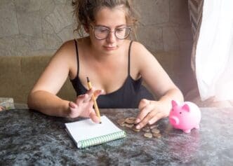 A young girl cries while looking at a piggy bank with only pennies, representing her financial struggles.
