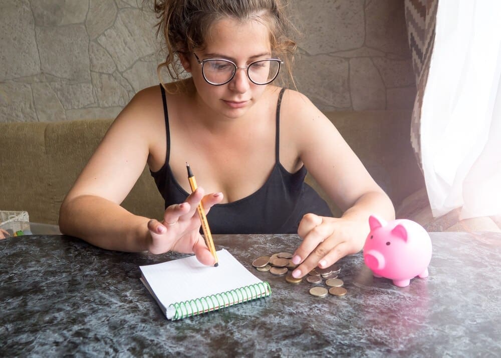 A young girl cries while looking at a piggy bank with only pennies, representing her financial struggles.