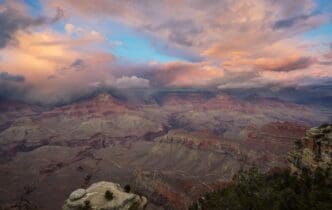 A wide-angle view showcases the vast, layered rock formations and deep gorges of the Grand Canyon, bathed in sunlight.