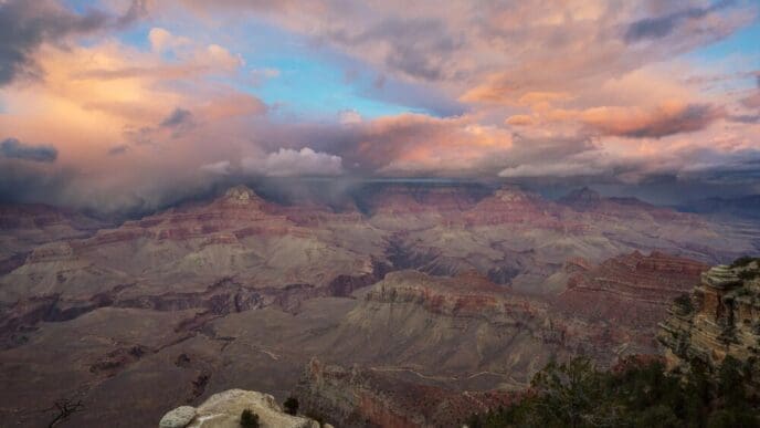 A wide-angle view showcases the vast, layered rock formations and deep gorges of the Grand Canyon, bathed in sunlight.