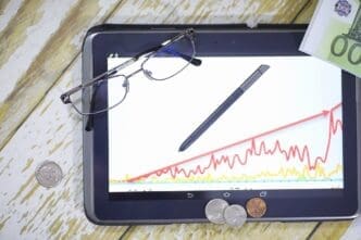 A person uses a tablet and smartphone to view a graph depicting income growth, with currency symbols visible on the chart.