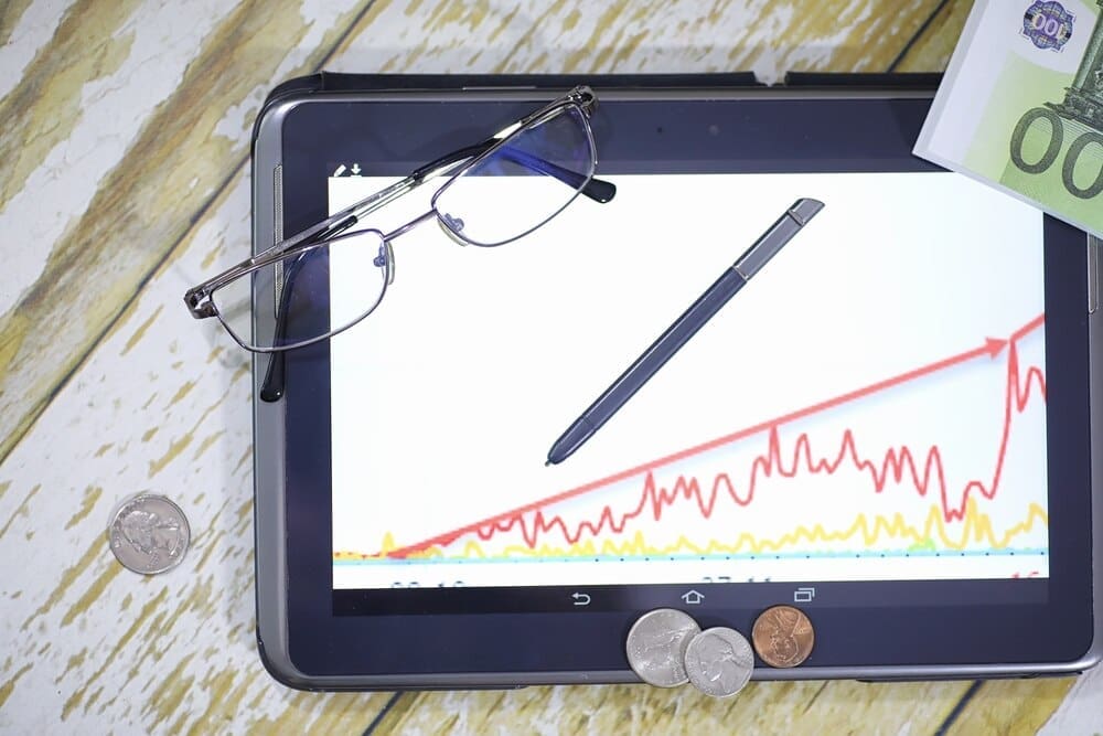 A person uses a tablet and smartphone to view a graph depicting income growth, with currency symbols visible on the chart.