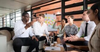 A diverse group of businesspeople brainstorm around a table, examining a small hand robot model.