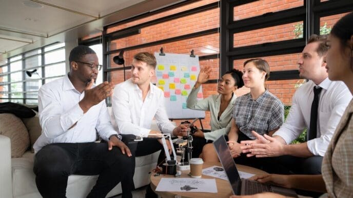 A diverse group of businesspeople brainstorm around a table, examining a small hand robot model.