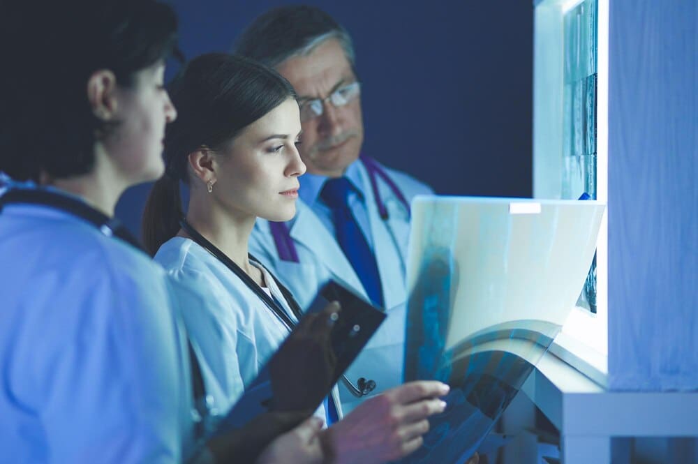 A group of medical professionals in a clinic examine X-rays, seemingly discussing a diagnosis.