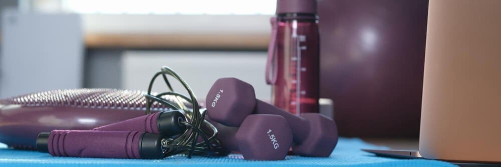 Close-up of various pieces of gym equipment, such as weights and exercise bands, arranged for a home workout.