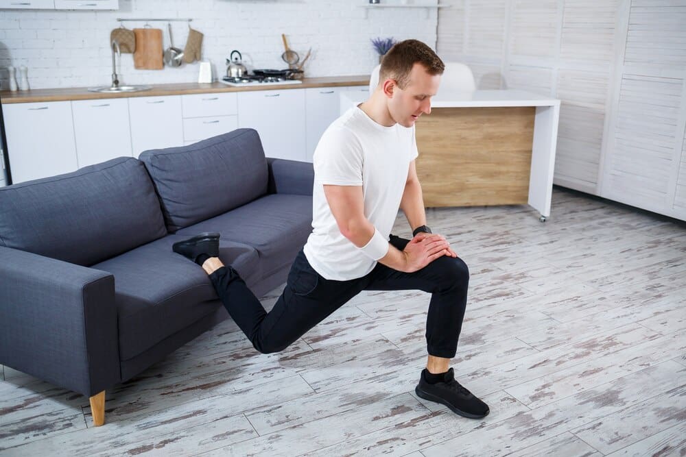 A fit man in a T-shirt squats in his apartment, demonstrating home fitness.