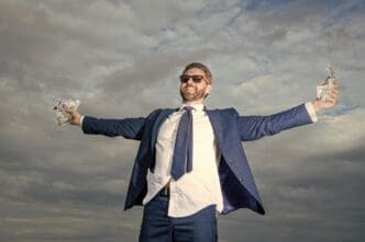 A smiling man in a suit holds money against a bright sky.