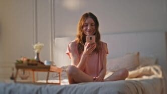 Happy teenage girl holding a phone, smiling, and looking at something off-screen while holding a heart-shaped object.