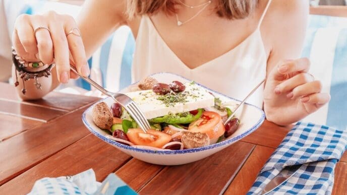 A smiling woman enjoys a Greek salad Horiatiki in a restaurant.