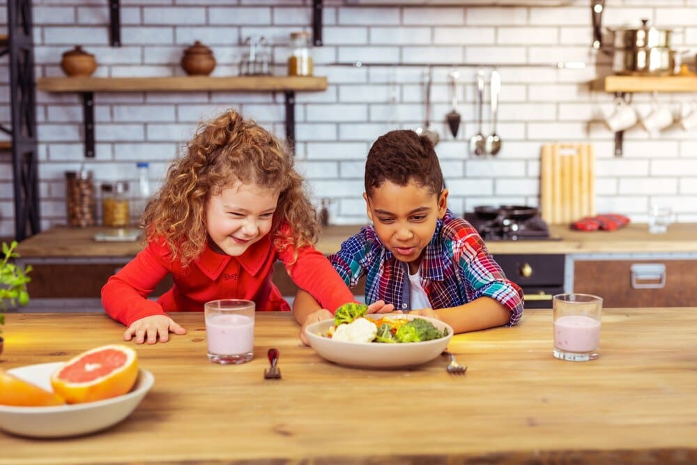 A frustrated young girl pushes away a bowl of broccoli.