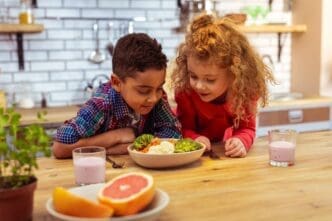 A young boy leans on a table with healthy food, appearing thoughtful.
