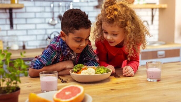 A young boy leans on a table with healthy food, appearing thoughtful.