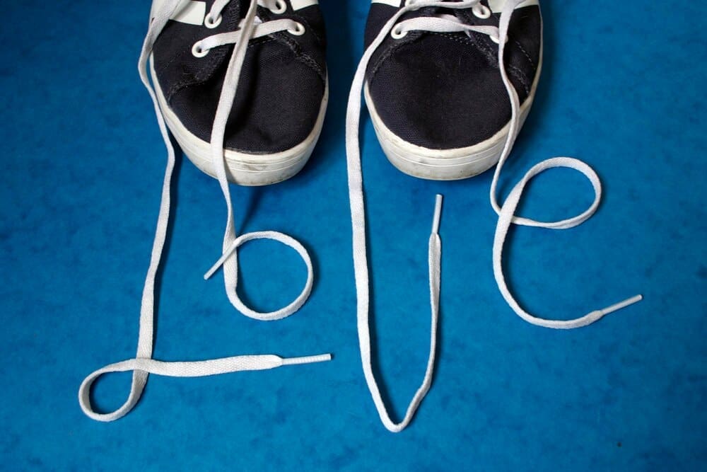 A high-angle shot shows the word "love" spelled out on a wooden floor using red shoelaces.