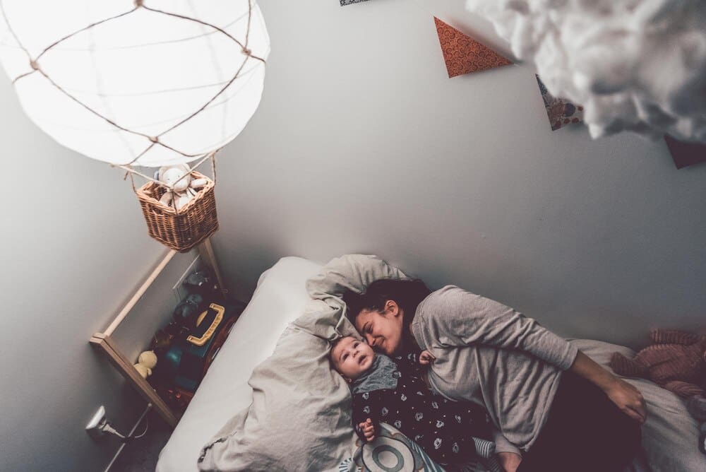 High-angle shot shows a mother and son lying on a bed together in a home setting.